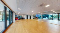 Located at 39 Bruton St in San Francisco, CA, this fitness and movement studio offers a thoughtfully designed, open-plan space ideal for group exercise, yoga, dance, and functional training. The studio features warm-toned hardwood flooring throughout, providing a durable yet inviting surface suited to a wide range of activities.

Full-length mirrors line multiple walls, enhancing the sense of spaciousness and allowing users to monitor their form during workouts. Recessed lighting in the acoustic tile ceiling ensures bright, even illumination across the entire floor. A dedicated equipment zone houses an organized rack system stocked with medicine balls, stability balls, resistance tools, a punching bag, and various functional training accessories, keeping the central floor area open and versatile.

A standout feature of this studio is the expansive floor-to-ceiling glass sliding wall that opens directly onto a landscaped outdoor courtyard. The courtyard, furnished with seating and mature trees, allows natural light to flood the interior and provides an option for indoor-outdoor training sessions. The clean, neutral-toned walls and modern finishes contribute to a professional yet welcoming atmosphere, making this studio a well-rounded facility for fitness and wellness programming.