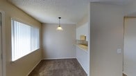This 2-bedroom, 2-bathroom single-floor residence offers a thoughtfully arranged layout that maximizes functionality and comfort. The living and dining areas are finished with warm neutral-toned carpeting and beige walls, creating a cozy and inviting atmosphere throughout. A decorative pendant light anchors the dining area, adding a touch of character to the space. Vertical blinds on the windows allow for flexible light control and privacy. A pass-through opening connects the dining area to the kitchen, promoting an open feel and easy interaction between spaces. The kitchen features this convenient pass-through counter, making it practical for everyday use. The textured popcorn ceiling is consistent throughout, giving the home a classic, familiar aesthetic. The single-floor plan ensures easy accessibility and seamless flow between rooms. With its neutral color palette and straightforward design, this residence offers a blank canvas that can be easily personalized to suit a variety of tastes and furnishing styles. The layout is well-suited for roommates, small families, or individuals seeking a comfortable and efficiently designed living space.