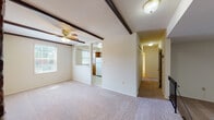 This single-floor residence offers a thoughtfully laid-out interior with a variety of distinctive architectural details. The main living area is characterized by decorative dark wood beam accents across the ceiling and a ceiling fan, lending the space a warm, classic character. A standout feature is the split-level design, where a raised living zone steps down via wrought iron-railed stairs to a lower lounge area anchored by a striking full-height exposed brick accent wall, adding texture and visual interest to the open layout. Large sliding glass doors in one of the living areas allow natural light to pour in while providing outdoor access. The kitchen is equipped with warm oak cabinetry extending to the upper walls, dark-toned countertops, a gas range, dishwasher, and refrigerator, all set on light tile flooring. A dedicated hallway leads to the bedroom wing, where the spacious primary bedroom features double closets with louvered bifold doors and multiple windows that bring in natural light. Additional carpeted rooms provide flexible living space. The bathroom includes a full tub/shower combination, a vanity with white cabinetry, and a mosaic tile floor. Throughout, neutral wall tones and plush carpeting create a cohesive and comfortable atmosphere.