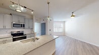 Located at 100 Harley Ln in Pooler, GA, this one-bedroom, one-bathroom residence offers a thoughtfully designed single-floor layout with modern finishes throughout. The open-concept kitchen and living area serves as the heart of the home, where a large granite-topped island with an undermount sink anchors the space. The kitchen features gray shaker-style cabinetry, a white subway tile backsplash, stainless steel appliances including a refrigerator, electric range, and over-the-range microwave, all illuminated by stylish pendant and track lighting. Light hardwood-style flooring flows seamlessly throughout the entire residence, lending a clean, cohesive aesthetic. The living area is bright and open, with a large window allowing natural light to fill the space. The bedroom is a comfortable size, with its own window offering views of the surrounding neighborhood and a ceiling fan for added comfort. A dedicated closet provides convenient storage. Gray panel-style interior doors add a contemporary accent throughout the hallway and adjoining rooms. The overall design is clean, modern, and move-in ready, making efficient use of the well-proportioned floor plan.