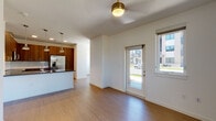 This single-floor residence offers a well-designed open-concept layout that seamlessly connects the living area to the kitchen. The living space features light wood-tone flooring, a ceiling fan with a brass-accented fixture, and a glass-panel exterior door that floods the area with natural light alongside a nearby window overlooking the surrounding neighborhood.

The kitchen is a standout feature, showcasing rich walnut-toned cabinetry that extends to the ceiling, a light-toned quartz island with an undermount sink and brass faucet, and a full suite of stainless steel appliances including a French door refrigerator, electric range, and built-in microwave. A subtle tile backsplash and pendant lighting with brass industrial-style fixtures complete the modern aesthetic.

The bedroom offers plush carpeting, a ceiling fan, and multiple windows providing generous natural light and open outdoor views of greenery and landscape. The bathroom features wood-look flooring, a soaking tub with large-format tile surround, a dark-toned vanity, and direct access to a walk-in closet with built-in shelving and hanging rods. Throughout, the space maintains a clean, contemporary ambiance with crisp white walls and cohesive modern finishes.