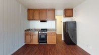 Located at 14 Casey Pl in Brockport, NY, this single-floor unit offers a practical and straightforward layout across two distinct living zones. The living area features rich, dark hardwood-style flooring that catches natural light streaming through a window fitted with blinds. A wall-mounted PTAC heating and cooling unit provides year-round climate control, and vertical shiplap-style wall paneling adds a touch of visual character to the space. The kitchen is efficiently designed, featuring warm wood cabinetry, granite-look countertops, a stainless sink, an electric range, and a full-size refrigerator, all set atop matching hardwood-style flooring. A private bedroom is carpeted for comfort and includes a baseboard heater, a window with blinds offering views of surrounding greenery, and clean white walls that create a calm, neutral atmosphere. The bathroom is clean and functional, with a single-sink vanity topped with a white countertop, a mirrored medicine cabinet, and a full-size bathtub and shower combination with tile flooring. Throughout the unit, the design is simple and practical, making it well-suited for those seeking a no-fuss living environment in the Brockport community.
