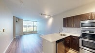 This efficiently designed 1-bedroom, 1-bathroom residence offers a thoughtful layout across a single floor, maximizing both comfort and functionality. The open-concept kitchen and living area serves as the heart of the home, anchored by a peninsula with a sleek stone countertop and undermount sink. The kitchen is equipped with rich dark-wood cabinetry, a classic white subway tile backsplash, and a full suite of stainless steel appliances, including a range, over-the-range microwave, dishwasher, and refrigerator. Track lighting overhead adds a modern touch to the space. The living area is bathed in natural light from a large floor-to-ceiling window, creating an airy, open ambiance, and features light wood-tone flooring that carries throughout the unit. The bedroom is a comfortable retreat with its own window offering outdoor views, a ceiling fan, and the same warm hardwood-style flooring. The bathroom includes a stone-topped vanity with dark cabinetry consistent with the kitchen's design. A stacked washer and dryer unit is conveniently housed within the unit. A dedicated closet provides additional storage, rounding out this well-organized and modern living space.