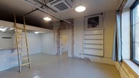 This single-floor commercial space offers a compelling mix of industrial character and clean, modern finishes. The open layout is anchored by polished concrete floors that lend a sleek, durable foundation throughout. Soaring ceilings expose structural ductwork and conduit, adding an authentic industrial aesthetic that is complemented by pendant lighting fixtures that cast warm, even illumination across the space.

Exposed brick accents appear prominently along the walls, framing doorways and adding rich texture and visual depth against the otherwise crisp white painted surfaces. Built-in white shelving units provide practical storage or display options, seamlessly integrated into the wall design. A cassette-style HVAC unit is mounted in the ceiling, ensuring efficient climate control throughout.

The space includes a separate enclosed room accessible through an interior door, offering flexible use as a private office, storage area, or additional workspace. The overall ambiance is open, airy, and adaptable, making it well-suited for a variety of commercial uses including retail, creative studio, office, or showroom purposes. The thoughtful combination of raw architectural elements and clean finishes creates an inviting, versatile environment with strong visual appeal.
