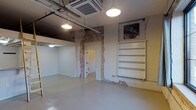 This single-floor commercial space offers a compelling mix of industrial character and clean, modern finishes. The open layout is anchored by polished concrete floors that lend a sleek, durable foundation throughout. Soaring ceilings expose structural ductwork and conduit, adding an authentic industrial aesthetic that is complemented by pendant lighting fixtures that cast warm, even illumination across the space.

Exposed brick accents appear prominently along the walls, framing doorways and adding rich texture and visual depth against the otherwise crisp white painted surfaces. Built-in white shelving units provide practical storage or display options, seamlessly integrated into the wall design. A cassette-style HVAC unit is mounted in the ceiling, ensuring efficient climate control throughout.

The space includes a separate enclosed room accessible through an interior door, offering flexible use as a private office, storage area, or additional workspace. The overall ambiance is open, airy, and adaptable, making it well-suited for a variety of commercial uses including retail, creative studio, office, or showroom purposes. The thoughtful combination of raw architectural elements and clean finishes creates an inviting, versatile environment with strong visual appeal.