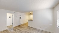 This efficiently laid-out 1-bedroom, 1-bathroom unit offers a clean, modern aesthetic across its single-floor design. Light wood-style flooring runs throughout, lending warmth and continuity to every room, while crisp white walls and textured ceilings create a bright, airy atmosphere.

The living room is a comfortable, open space featuring a wall-mounted air conditioning unit and a window fitted with blinds that allows natural light to filter in. A pass-through counter with a dark countertop connects the living area to the kitchen, enhancing the sense of openness between the two spaces.

The galley-style kitchen is well-appointed, featuring white shaker cabinetry, grey countertops, a stainless steel sink, and a full suite of stainless steel appliances including a gas range, microwave, and refrigerator. Track lighting and a window overlooking the exterior provide both function and brightness.

The bedroom is a serene, comfortably sized retreat equipped with a ceiling fan, a wide window with blinds for natural light, and a mirrored sliding closet door that adds depth to the room.

The bathroom includes a full soaking tub with a showerhead, white tile surrounds, and a frosted window that brings in soft natural light while maintaining privacy. A connecting hallway ties the layout together seamlessly.