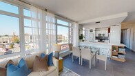 Located at 199 2nd Street in Mineola, NY, this single-floor residence at Morgan Parc showcases a contemporary design defined by clean lines, abundant natural light, and a cohesive neutral palette throughout. Floor-to-ceiling windows in the open-concept living and dining area frame sweeping views of the surrounding Mineola streetscape, flooding the space with sunlight and creating an airy, elevated ambiance. Sheer white curtains add a soft, elegant touch to the expansive glazing.

The living area flows seamlessly into a well-appointed kitchen featuring white cabinetry, warm wood accents, a grey subway tile backsplash, and a full suite of stainless steel appliances, including a double oven range and built-in microwave. Large-format grey tile flooring unifies the common areas.

The entryway makes a distinct impression with a decorative living plant wall display and a console table, setting a welcoming tone. Bedrooms are generously sized with large windows offering outdoor views. The primary bedroom enjoys abundant natural light, while a secondary bedroom provides flexible accommodations.

Bathrooms are finished with floor-to-ceiling marble-look tile, backlit mirrors, and modern fixtures, including a glass-enclosed shower in one and a soaking tub combination in another.