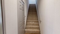This three-story home offers a thoughtfully organized layout spread across three distinct levels. The ground floor houses an attached garage equipped with an automatic opener, providing convenient and secure parking alongside additional storage space.

The main living level features a bright, open-concept area that seamlessly integrates the living room and kitchen. Light wood-look flooring, crown molding with gray trim accents, and ceiling fans lend the space a clean, contemporary feel. The kitchen is outfitted with stainless steel appliances—including a range, over-the-range microwave, and French door refrigerator—complemented by gray shaker-style cabinetry, white countertops, and a decorative tile backsplash. A central island adds prep space and visual definition. A half bathroom with a gray vanity and white countertop is also found on this level. Carpeted staircases connect all three floors.

The upper level hosts all three bedrooms, including a generously sized primary bedroom featuring plush carpet, a ceiling fan, and direct access to an en suite bathroom. The primary bath offers a dual-sink vanity with ample cabinetry, a large mirror, and tile flooring. Additional bedrooms provide comfortable proportions with carpet flooring and access to closet storage. A dedicated laundry area and hallway spaces complete the upper level, making this home both functional and well-suited for everyday living.