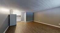 Located at 401 NW 64th St in Gladstone, Missouri, this efficiently designed single-floor unit offers a practical and comfortable layout. The main living area is open and inviting, featuring warm hardwood-style vinyl plank flooring that runs throughout the space, complemented by neutral gray walls and crisp white baseboards that create a clean, modern aesthetic. A textured ceiling adds a classic touch overhead.

The living area is well-lit by a front-facing window that allows natural light to filter in, and includes a wall-mounted HVAC unit for year-round climate control. A paneled entry door provides direct access to the unit.

The kitchenette is neatly integrated into the layout, featuring white cabinetry, a countertop workspace, a refrigerator, a range, and a sink — offering all the essentials for everyday meal preparation in a compact footprint.

A closet area with built-in hanging rods provides convenient storage. The bathroom is well-appointed with white cabinetry, a vanity with sink, and a bathtub, maintaining the same clean, white-accented design found throughout the rest of the unit.

Overall, this unit presents a functional and cohesive living space with consistent finishes, making it a straightforward and practical option in the Gladstone area.