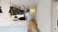Located at 200 Nursery Lane in Fort Worth, Texas, this 2-bedroom, 1-bathroom unit offers a thoughtfully designed layout that maximizes every square foot of its single-floor footprint. The kitchen serves as a standout feature, showcasing rich dark espresso cabinetry, granite-style countertops, stainless steel appliances including a refrigerator, range, and microwave, and stylish pendant lighting over a breakfast bar peninsula. Wood-look flooring runs throughout the main living and kitchen areas, lending warmth and continuity to the space. A connecting hallway leads from the kitchen toward the bedrooms, providing a clear and functional flow throughout the unit. Both bedrooms are carpeted and brightened by natural light from windows fitted with blinds, and each includes a ceiling fan. The primary bedroom features a walk-in closet with built-in shelving and hanging rods, offering ample storage. The bathroom is finished with large-format dark tile in the tub/shower surround, wood-look flooring, a dark-cabinetry vanity with a granite-style countertop, a framed mirror, and brushed nickel hardware. The two-panel interior doors and clean white walls throughout contribute to a cohesive, contemporary aesthetic that defines this efficient Fort Worth residence.