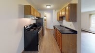 This single-floor unit offers a practical and functional layout across several well-defined living areas. The main living space features warm wood-look laminate flooring, neutral cream-toned walls, and vertical blinds covering a large sliding glass door that allows natural light to fill the room. A wall-mounted air conditioning unit and baseboard heating provide year-round climate control throughout the space.

The galley-style kitchen is equipped with warm oak cabinetry offering generous upper and lower storage, dark countertops, a double basin sink, and stainless steel appliances including an electric range and refrigerator. A textured ceiling and overhead lighting complete the functional workspace, which connects conveniently to the rest of the unit.

The bedrooms are finished with plush carpeting, neutral walls, and vertical blinds over windows that bring in natural light. Each bedroom benefits from baseboard heating and dedicated closet space, with at least one room featuring a walk-in closet with built-in shelving and hanging rod.

Two full bathrooms serve the unit, each featuring white square tile flooring, a tiled tub-shower combination, a toilet, and a vanity with sink. The clean, all-white aesthetic creates a bright and tidy atmosphere. Overall, the unit presents a straightforward, well-maintained living environment suitable for comfortable everyday living.