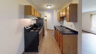 This single-floor unit offers a practical and functional layout across several well-defined living areas. The main living space features warm wood-look laminate flooring, neutral cream-toned walls, and vertical blinds covering a large sliding glass door that allows natural light to fill the room. A wall-mounted air conditioning unit and baseboard heating provide year-round climate control throughout the space.

The galley-style kitchen is equipped with warm oak cabinetry offering generous upper and lower storage, dark countertops, a double basin sink, and stainless steel appliances including an electric range and refrigerator. A textured ceiling and overhead lighting complete the functional workspace, which connects conveniently to the rest of the unit.

The bedrooms are finished with plush carpeting, neutral walls, and vertical blinds over windows that bring in natural light. Each bedroom benefits from baseboard heating and dedicated closet space, with at least one room featuring a walk-in closet with built-in shelving and hanging rod.

Two full bathrooms serve the unit, each featuring white square tile flooring, a tiled tub-shower combination, a toilet, and a vanity with sink. The clean, all-white aesthetic creates a bright and tidy atmosphere. Overall, the unit presents a straightforward, well-maintained living environment suitable for comfortable everyday living.
