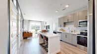 Located at 2200 Cascade Pointe Blvd in Charlotte, NC, this well-appointed 2-bedroom, 2-bathroom residence offers a thoughtfully designed open-concept floor plan finished with light wood-style flooring throughout. The kitchen serves as a central hub, showcasing taupe cabinetry with matte black hardware, a subway tile backsplash, stainless steel appliances, and a white-topped island with bar seating — seamlessly connecting to the living area. The living room is anchored by a bold dark accent wall and floor-to-ceiling sliding glass doors that flood the space with natural light and open to a private outdoor patio with neighborhood views. The spacious primary bedroom features large windows, generous closet space, and a serene, neutral palette. Its en-suite bathroom is equipped with a wood-toned vanity and walk-in closet with built-in shelving. The second bathroom offers a full tiled tub-shower combination with a matching vanity. A hallway connects all rooms, maintaining a clean and efficient layout. The overall ambiance is modern and bright, with consistent contemporary finishes creating a cohesive, comfortable living environment throughout.