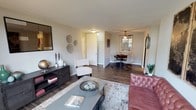 This single-floor residence offers a thoughtfully arranged layout that balances comfort and functionality. The open-concept living and dining area is anchored by dark hardwood-style flooring, neutral gray walls, and ample natural light streaming in through large windows. The living area provides generous space for seating arrangements, while the adjacent dining space accommodates a full table and chairs beneath a ceiling fan, creating a cohesive, relaxed atmosphere.

The kitchen is well-appointed with warm cherry wood cabinetry, dark granite countertops, a white subway tile backsplash, and stainless steel appliances including a gas range, microwave, refrigerator, and a stainless sink — offering both style and practicality.

The primary bedroom is carpeted and features large sliding glass doors that flood the room with natural light and provide outdoor views. A second bedroom, equally well-lit by a sizable window, offers versatile use as a guest room or home office.

The walk-in closet is a notable feature, equipped with wire shelving on multiple walls and a window that brightens the space. The bathroom includes a granite-topped vanity, a large mirror, and a tiled tub-shower combination, completing this well-designed residence.