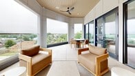 Located at 505 W 8th St in Dallas, Texas, this thoughtfully designed single-floor lounge space offers a seamless blend of modern interior elegance and open-air living. The interior living area features light hardwood flooring, recessed lighting, and warm neutral tones accented by taupe wood paneling on the walls. A plush seating arrangement anchors the space, complemented by cognac leather accent chairs, a sculptural coffee table, and a built-in media console finished in natural wood with a white marble top. Lush greenery adds a refreshing, organic touch throughout.

Large floor-to-ceiling black-framed glass sliding doors connect the interior to a generous wraparound outdoor terrace, flooding the space with abundant natural light and offering sweeping views of the surrounding Dallas skyline and treetops. The terrace itself is finished with large-format tile and features a curved architectural ceiling with wood-paneled detailing and a ceiling fan, creating a comfortable al fresco environment. Lounge seating and a dining table with chairs make this outdoor area ideal for both relaxation and entertaining. Together, the two living zones create a cohesive, airy atmosphere that balances sophisticated design with functional, inviting comfort.