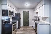 This 2-bedroom, 1-bathroom unit in Memphis, Tennessee offers a clean, modern interior finished with consistent light wood-look flooring throughout. The open layout connects the living area to the kitchen, which features white shaker-style cabinetry, granite-look countertops, stainless steel appliances including a refrigerator and dishwasher, and a black undermount sink — all complemented by a distinctive sage green exterior door. Neutral gray walls and crisp white trim create a bright, cohesive aesthetic across the entire space. Both bedrooms are comfortably sized, bathed in natural light from windows fitted with blinds, and include closets with wire shelving for organized storage. The bathroom is outfitted with a full tub-shower combo surrounded by white tile, a classic black-and-white mosaic tile floor, and a granite-topped vanity. Ceiling vents and recessed lighting ensure year-round comfort and well-distributed illumination. The unit's single-floor layout provides efficient, straightforward flow between rooms, making it a practical and attractive living space in the 38111 zip code of Memphis.