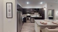 This thoughtfully designed single-floor residence offers a cohesive blend of modern aesthetics and functional living spaces. The kitchen serves as a standout feature, boasting rich dark cabinetry, stainless steel appliances including a French door refrigerator, microwave, range, and dishwasher, paired with granite countertops and a classic subway tile backsplash. Light wood-style flooring runs throughout the main areas, adding warmth and continuity. A breakfast bar provides casual dining space, complementing the open flow between the kitchen and living areas. The living room is bright and welcoming, with natural light streaming through large windows dressed with blinds and curtain panels, creating a comfortable and inviting atmosphere. The primary bedroom features plush carpeting, a ceiling fan, and generous natural light, with direct access to a walk-in closet equipped with built-in shelving and hanging rods. The en-suite bathroom includes a dark-toned vanity with granite countertops and a soaking tub with shower combination finished in clean white tile. The second bedroom mirrors the comfort of the primary, also featuring a ceiling fan and ample natural light. Both bedrooms offer a calm, restful ambiance with neutral tones throughout, making this residence a well-rounded and inviting home.