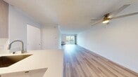 This 570 square foot apartment in Newport Beach offers a thoughtfully designed living space that maximizes functionality and style. The open-concept floor plan seamlessly integrates the living room and kitchen, creating a spacious feel despite the compact footprint. Light wood flooring throughout adds warmth and continuity to the space.

The kitchen is a standout feature, boasting sleek white cabinetry, stainless steel appliances, and a practical island with a sink, perfect for meal preparation or casual dining. The living area is bathed in natural light thanks to large sliding glass doors that lead to a private balcony, offering a connection to the outdoors.

Clever storage solutions are incorporated throughout, including a mirrored sliding door closet in the bedroom area, which not only provides ample storage but also visually expands the space. The bathroom, while not pictured, likely continues the modern aesthetic found throughout the apartment.

Additional amenities include baseboard heating and an in-window air conditioning unit for year-round comfort. The neutral color palette and clean lines create a canvas for personalizing the space to individual tastes. This apartment is ideal for those seeking a contemporary living experience in a prime Newport Beach location.