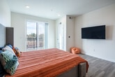 This well-appointed single-floor unit offers a thoughtfully designed layout that maximizes both functionality and comfort. The open-concept kitchen is a standout feature, showcasing crisp white shaker cabinetry, dark granite countertops, a classic white subway tile backsplash, and a full suite of stainless steel appliances including a gas range, built-in microwave, dishwasher, and refrigerator. Open shelving adds a modern touch, while a compact dining area with a round table and chairs sits conveniently adjacent, making the space ideal for everyday living. Light wood-tone flooring flows consistently throughout, lending warmth and visual continuity across all areas. A hallway connects the main living spaces to the bedroom and bathroom, with recessed lighting providing clean, even illumination. The bedroom is spacious and airy, benefiting from large sliding glass doors that open to a private balcony, flooding the room with natural light and offering outdoor views. The bathroom is elegantly finished with a rich walnut-toned vanity, white quartz countertop, a backlit rectangular mirror, and a frameless glass walk-in shower. Decorative patterned tile flooring in the bathroom adds a distinctive design element, complementing the overall contemporary aesthetic of the unit.
