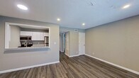 This single-floor unit offers a clean, modern design with a functional and open layout. The main living area is bright and welcoming, featuring warm hardwood-style flooring, neutral gray-toned walls, and recessed lighting throughout. Two windows along the front wall invite natural light into the space, creating an airy and comfortable atmosphere. Clean white baseboards provide a crisp contrast to the flooring and walls.

The kitchen is accessible via a pass-through counter that opens directly into the living area, enhancing the open-concept flow. It is outfitted with white shaker-style cabinetry, granite countertops, and stainless steel appliances including an electric range, over-the-range microwave, and refrigerator. The textured ceiling adds a classic touch present throughout the unit.

A hallway connects the living space to the additional rooms, including a full bathroom. The bathroom features a tub-shower combination with white tile surround, a toilet, a vanity with a light countertop, and a mirror. The same hardwood-style flooring extends into this space as well.

Overall, the unit presents a cohesive, move-in-ready aesthetic with consistent finishes, practical storage options, and a straightforward, well-organized floor plan suitable for everyday living.