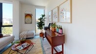 This contemporary single-floor residence offers a well-designed layout that balances modern aesthetics with functional living. Light wood flooring flows throughout, unifying each space with a clean, cohesive look.

The entryway sets an inviting tone with a compact desk area accented by wall-mounted shelving displaying lush greenery and succulents, alongside a louvered closet door that adds textural interest. A bright hallway connects the rooms, adorned with framed artwork and recessed lighting.

The kitchen is sleek and modern, featuring floor-to-ceiling white cabinetry with under-cabinet lighting, a copper-toned sink, stainless steel appliances, and ample counter space — ideal for both everyday cooking and entertaining.

The living area benefits from a tall vertical window that fills the room with natural light and urban views, complemented by warm mid-century modern furnishings and vibrant wall art.

Both bedrooms are generously sized, with one showcasing expansive floor-to-ceiling windows framing outdoor city and treetop views, flooding the space with sunlight. The second bedroom offers a cozy, stylishly appointed retreat.

Two full bathrooms feature large-format tile flooring, soaking tubs with shower combinations, open vanities with illuminated mirrors, and a clean, neutral palette throughout.