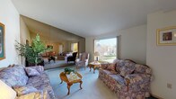 Located at 1015 East Cozza Drive, Unit 35 in Spokane, WA, this single-floor residence offers a well-organized layout with comfortable living spaces throughout. The expansive living room is a standout, featuring vaulted ceilings, plush carpeting, and a large picture window that fills the room with natural light and provides views of the surrounding greenery. A full-wall mirror accent amplifies the sense of space and brightness. The galley-style kitchen is efficiently designed with white cabinetry, white appliances including a refrigerator and dishwasher, and a double sink, opening directly into the adjacent dining area. The dining space is lit by track lighting and offers room for a four-person table, with views into the kitchen for easy entertaining. The primary bedroom is a calm, carpeted retreat with a wall-mounted AC unit, while the second bedroom features a sliding closet and ample natural light. The bathroom includes a soaking tub with tile surround, and a separate vanity area with a wide mirror and bright overhead lighting. Additional utility storage with a water heater is conveniently tucked nearby, rounding out this practical and comfortable Spokane residence.
