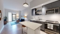 Located at 801-901 H St NE in Washington, DC, this two-bedroom, one-bathroom unit offers a well-designed open-concept layout with contemporary finishes throughout. The kitchen is a standout feature, equipped with dark charcoal flat-front cabinetry, white quartz countertops, a subway tile backsplash, stainless steel appliances, and a central island with bar seating — all illuminated by a stylish pendant light. Light wood-style flooring flows seamlessly from the kitchen into the living area, which benefits from elevated ceilings and a glass door opening to a private outdoor space, filling the room with natural light. The primary bedroom is a comfortable retreat, featuring large windows with outdoor views, hardwood-style flooring, and generous closet space with adjustable shelving. The second bedroom is bright and efficiently laid out. The shared bathroom is finished with large-format dark tile flooring and clean white cabinetry. Throughout the unit, the neutral color palette, modern fixtures, and thoughtful layout create a cohesive, contemporary ambiance well-suited for urban living in one of DC's most vibrant neighborhoods.