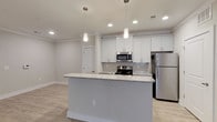 The Blossom floor plan is a well-appointed single-story, 3-bedroom, 2-bathroom residence designed with comfort and functionality in mind. The open-concept kitchen serves as a central highlight, featuring white shaker-style cabinetry, granite countertops, a subway tile backsplash, and stainless steel appliances including a range, microwave, and refrigerator. A spacious kitchen island with a granite surface and undermount sink provides additional prep space and casual seating, illuminated by stylish pendant lighting overhead. Recessed lighting and light wood-look luxury vinyl plank flooring extend throughout the main living areas, creating a bright and cohesive atmosphere. The generously sized living area offers ample room for a variety of furniture arrangements and features a ceiling fan for added comfort. Each of the three bedrooms is carpeted and includes a ceiling fan and windows with blinds that allow for natural light. The two bathrooms are finished with tile flooring, granite-topped vanities with dark cabinetry, and tub-shower combinations. Neutral tones, clean white trim, and crown molding detail throughout lend the space a polished, move-in-ready appeal.