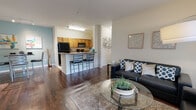 Located at 2614 W Tennessee Street in Tallahassee, Florida, this single-floor residence offers a well-designed, open-concept layout with rich hardwood-style flooring flowing throughout the main living areas. The living room is bright and spacious, featuring a ceiling fan, large sliding glass doors that invite natural light and provide outdoor views, and ample space for comfortable seating arrangements.

The kitchen is thoughtfully appointed with warm wood cabinetry, granite-style countertops, black appliances including a refrigerator, range, and microwave, and a breakfast bar that seats multiple guests. An adjacent dining area with track lighting adds versatility to the entertaining space.

The primary bedroom features a bold accent wall, plush carpeting, a ceiling fan, and generous natural light from large windows with outdoor views. The en-suite bathroom offers a granite-topped vanity with wood cabinetry and an oversized garden-style bathtub. A second bedroom is equally well-lit with large windows and soft carpeting. The second full bathroom mirrors the quality of the first, with a matching granite vanity and tile flooring.

Additional conveniences include an in-unit laundry area with a full-size washer. The overall ambiance is warm and inviting, combining practical functionality with comfortable, residential design throughout.