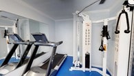 Located at 6413 Ashborough Ct in Milton, Florida, this dedicated fitness space is thoughtfully designed to support a full range of exercise routines. The single-level layout is finished with durable blue rubber flooring, light gray walls, and crisp white crown molding, creating a clean and energizing environment conducive to focused training.

The space is outfitted with an impressive selection of equipment. Cardio offerings include a treadmill, an Octane elliptical trainer, and a recumbent stationary bike, providing options for varied aerobic workouts. A multi-functional HD cable machine serves as the centerpiece for strength training, accommodating a wide variety of resistance exercises. A tiered dumbbell rack stocked with multiple weight increments rounds out the free weight offerings, supporting both light toning and heavier lifting.

A large wall-mounted mirror spans one side of the room, visually expanding the space and allowing users to monitor their form during exercise. A wall-mounted flat-screen television adds an entertainment element, making longer workout sessions more enjoyable. Natural light filters in through a window fitted with horizontal blinds, while a glass-panel exterior door provides easy access and additional brightness. The overall ambiance is practical and polished, reflecting a space purpose-built for consistent, versatile physical training.