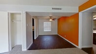This single-floor residence makes a striking visual impression with its bold orange and golden-yellow accent walls that punctuate the neutral gray tones throughout. The living areas feature rich, dark hardwood-style flooring that flows seamlessly through the main spaces, while plush carpeting adds warmth to the bedrooms. Ceiling fans are installed throughout the home, enhancing both comfort and airflow in each room.

The kitchen is well-appointed with dark cabinetry, a mosaic glass tile backsplash in earthy tones, a double-basin sink, and a full-size refrigerator. Open shelving beside the kitchen adds functional storage and visual interest. The kitchen connects naturally to the main living area, which offers a generous, open feel with access to natural light through windowed walls.

The bedrooms are comfortably sized, each featuring carpet flooring, ceiling fans, and windows fitted with horizontal blinds that allow for natural light and privacy. Closet access is provided in the bedrooms, offering practical storage solutions.

The bathrooms mirror each other in design, each showcasing a sleek dark-framed vanity mirror, a white quartz countertop with an undermount sink, dark lower cabinetry with modern hardware, and a coordinating mosaic tile accent band that ties back to the kitchen's design aesthetic. Dark hardwood-style flooring extends into the bathrooms, maintaining a cohesive look throughout the home.
