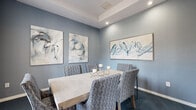 Located at 600 River Birch Ct in Clermont, Florida, this single-floor space offers a refined and cohesive interior design experience across its well-appointed layout. The space is divided into two primary areas: a stylish dining room and a spacious open living area, each showcasing thoughtful design details.

The dining room is adorned with cool steel-blue walls that create a calm, sophisticated atmosphere. A tray ceiling with recessed lighting adds architectural depth, while large windows dressed with patterned drapes and plantation shutters invite natural light and views of the outdoors. French doors connect the dining room to the broader space, enhancing its sense of openness. Abstract wall art in coordinating blue and white tones complements the room's palette, and plush blue carpeting anchors the seating arrangement.

The living area presents a striking contrast with wide-plank hardwood flooring that stretches across a generously proportioned open floor plan. Soaring ceilings are punctuated by an elegant geometric pendant chandelier, while large windows and glass doors flood the room with natural light. Soft neutral tones on the walls, paired with curated seating arrangements, create a welcoming and versatile gathering space. Together, both areas reflect a polished, cohesive aesthetic with upscale community-oriented design throughout.