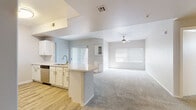 This single-floor home offers a thoughtfully designed open-concept layout that seamlessly connects the kitchen and living area. The kitchen is well-equipped with white cabinetry, light countertops, stainless steel appliances including a refrigerator, range, microwave, and dishwasher, and wood-look tile flooring. A peninsula with a sink provides both additional workspace and a natural divider between the kitchen and the expansive carpeted living room, which features a ceiling fan and multiple windows fitted with blinds that invite natural light throughout the day. The bedrooms are generously sized, each carpeted and brightened by natural light through window blinds. The primary suite includes access to a spacious walk-in closet outfitted with built-in shelving and hanging rods on multiple walls, offering substantial storage capacity. The primary bathroom features a wide vanity with white cabinetry, a mirror, and wood-look tile flooring that extends to a separate tub and shower area. A second full bathroom mirrors this clean, neutral aesthetic. A dedicated laundry room houses a full-size washer and dryer and includes a utility shelf and a small window. Throughout the home, a consistent neutral color palette, clean finishes, and wood-look tile and plush carpet flooring create a cohesive and move-in ready environment.