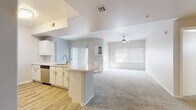 This single-floor home offers a thoughtfully designed open-concept layout that seamlessly connects the kitchen and living area. The kitchen is well-equipped with white cabinetry, light countertops, stainless steel appliances including a refrigerator, range, microwave, and dishwasher, and wood-look tile flooring. A peninsula with a sink provides both additional workspace and a natural divider between the kitchen and the expansive carpeted living room, which features a ceiling fan and multiple windows fitted with blinds that invite natural light throughout the day. The bedrooms are generously sized, each carpeted and brightened by natural light through window blinds. The primary suite includes access to a spacious walk-in closet outfitted with built-in shelving and hanging rods on multiple walls, offering substantial storage capacity. The primary bathroom features a wide vanity with white cabinetry, a mirror, and wood-look tile flooring that extends to a separate tub and shower area. A second full bathroom mirrors this clean, neutral aesthetic. A dedicated laundry room houses a full-size washer and dryer and includes a utility shelf and a small window. Throughout the home, a consistent neutral color palette, clean finishes, and wood-look tile and plush carpet flooring create a cohesive and move-in ready environment.