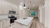 The Sugarloaf Grove Type A4 is a thoughtfully designed 1-bedroom, 1-bathroom residence located in Lawrenceville, GA. The open-concept layout seamlessly connects the kitchen and living area, creating an inviting and functional space. The kitchen is a standout feature, boasting a granite-topped center island with a built-in sink and dishwasher, stainless steel appliances including a refrigerator, electric range, and microwave, and light wood-toned cabinetry complemented by a classic subway tile backsplash. Three sleek pendant lights hang above the island, adding a modern touch. The living area extends naturally from the kitchen, featuring light wood-style flooring, a ceiling fan, and a window that brings in natural light and outdoor views. The bedroom is a comfortable retreat with the same wood-style flooring, a ceiling fan, and direct access to a private outdoor space through a glass door. A generously sized walk-in closet off the bedroom offers wire shelving and soft carpet underfoot. The bathroom is clean and contemporary, featuring granite countertops, a tub-shower combination with tile surround, and wood-style flooring, all finished in a bright, neutral palette throughout.