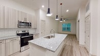 The Sugarloaf Grove Type A4 is a thoughtfully designed 1-bedroom, 1-bathroom residence located in Lawrenceville, GA. The open-concept layout seamlessly connects the kitchen and living area, creating an inviting and functional space. The kitchen is a standout feature, boasting a granite-topped center island with a built-in sink and dishwasher, stainless steel appliances including a refrigerator, electric range, and microwave, and light wood-toned cabinetry complemented by a classic subway tile backsplash. Three sleek pendant lights hang above the island, adding a modern touch. The living area extends naturally from the kitchen, featuring light wood-style flooring, a ceiling fan, and a window that brings in natural light and outdoor views. The bedroom is a comfortable retreat with the same wood-style flooring, a ceiling fan, and direct access to a private outdoor space through a glass door. A generously sized walk-in closet off the bedroom offers wire shelving and soft carpet underfoot. The bathroom is clean and contemporary, featuring granite countertops, a tub-shower combination with tile surround, and wood-style flooring, all finished in a bright, neutral palette throughout.
