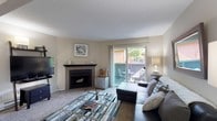 This single-floor residence offers a thoughtfully designed layout that balances comfort and functionality across its key living spaces. The living room serves as the heart of the home, featuring a corner fireplace with a classic black surround, soft carpeted flooring, and a textured ceiling. A sliding glass door floods the space with natural light and opens directly onto a private balcony, offering pleasant outdoor views of surrounding greenery. The living area flows seamlessly into a separate dining space, providing a natural separation that enhances the open feel of the floor plan. The galley-style kitchen is efficiently arranged with ample white cabinetry, neutral countertops, wood-look flooring, and black appliances including a refrigerator, range, and dishwasher. Two bedrooms offer quiet retreats, each with plush carpeting and windows that bring in natural light. The primary bedroom includes an en-suite bathroom with a single-sink vanity featuring white cabinetry and wood-look flooring. A second full bathroom mirrors the clean, neutral aesthetic with a tub-shower combination and similar vanity finishes. Throughout the residence, a consistent warm, neutral color palette and wood-look flooring in wet areas contribute to a cohesive and inviting ambiance.
