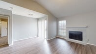 This single-story home presents a thoughtfully designed layout with a blend of functional and aesthetic elements throughout. The living room serves as a central highlight, featuring vaulted ceilings that enhance the sense of openness and a tile-surround fireplace with a white mantel as a focal point. Wood-look flooring extends across this space, and a sliding glass door with vertical blinds allows natural light to flow in while providing outdoor access. A separate dining or flex area adjoins the living room under standard ceiling height, creating a natural transition.

The kitchen is equipped with gray shaker-style cabinetry, quartz-style countertops, stainless steel appliances including a refrigerator and dishwasher, and a pass-through window that connects to the main living area. Wood-look flooring continues here, complementing the neutral color palette.

The bedrooms are carpeted and feature ceiling fans, natural light from windows with blinds, and walk-in or reach-in closets with built-in shelving. The bathrooms each include a tub-shower combination with white tile surround, wood-look flooring, and gray cabinetry with brushed gold hardware, maintaining a cohesive, modern aesthetic throughout the home.