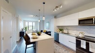 Located at 520 N Andrews Ave in Fort Lauderdale, FL, this single-floor residence showcases a contemporary design with an open-concept layout that seamlessly connects the kitchen, dining, and living areas. The kitchen is outfitted with sleek, flat-front white cabinetry extending to the ceiling, a marble-style tile backsplash, stainless steel appliances including a French door refrigerator and dishwasher, and a center island with bar seating — ideal for casual dining and entertaining. Pendant lighting and track fixtures illuminate the space, which flows directly into the living area, where large windows draw in generous natural light and offer outdoor views.

The living room provides a comfortable, open setting with wood-style flooring that carries throughout the unit. A secondary room features a bold accent wall and an additional window with outdoor views, offering versatility as a bedroom or den. The primary bedroom is distinguished by floor-to-ceiling windows that frame treetop views, creating a bright, airy retreat. The bathroom is finished with large-format marble-style tile flooring, a floating wood-tone vanity with open shelving, a white quartz countertop, and a backlit mirror, with a glass-enclosed shower visible beyond.