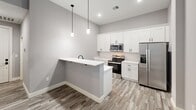 Located at 1230 Elm St in Manchester, NH, this one-bedroom, one-bathroom unit offers a thoughtfully designed layout that maximizes every square foot. The open-concept kitchen and living area serves as the heart of the home, featuring sleek white shaker cabinetry, a white subway tile backsplash, quartz-style countertops, and a full suite of stainless steel appliances including a range, microwave, and refrigerator. A peninsula with pendant lighting above provides additional prep space and casual seating. Light wood-style flooring runs throughout the main living areas, lending a clean, contemporary feel. The bedroom is a comfortable, carpeted retreat with a large window that frames views of the surrounding neighborhood, allowing natural light to fill the space. A closet with built-in shelving and an in-unit washer/dryer add everyday convenience. The bathroom is well-appointed with a white vanity, modern matte black hardware, a full tub/shower combination, and coordinating wood-style flooring that ties the aesthetic together. Neutral gray tones throughout the unit create a calm, cohesive ambiance, making this a polished and move-in-ready space in the heart of Manchester.