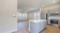 This two-story home offers four bedrooms and three bathrooms across two evenly divided floors, presenting a well-organized and functional layout. The ground floor opens into a combined kitchen and living area finished with light wood-style luxury vinyl flooring that extends throughout the main level. The kitchen is equipped with gray shaker-style cabinetry, a white quartz center island, stainless steel appliances including a French door refrigerator, and a window above the sink that brings in natural light. The open living area features recessed lighting, a ceiling fan, and multiple windows fitted with blinds, creating a bright and airy atmosphere. A staircase leads to the upper floor, where the four bedrooms are carpeted and include ceiling fans with recessed lighting. The primary bedroom is a comfortable size and connects to a dedicated bathroom featuring a granite-topped vanity with gray cabinetry, a glass-enclosed shower, tile flooring, and dual windows. A spacious walk-in closet with built-in shelving and hanging rods serves the primary suite. Additional bathrooms include a full tub-shower combo with large-format tile surround and brushed gold fixtures, maintaining a consistent, modern finish throughout the home.