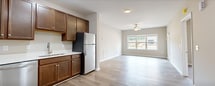 Located at 23 Encanto Ln, Unit 107 in Rustburg, VA, this single-story residence offers 1,130 square feet of thoughtfully designed living space across 3 bedrooms and 2 bathrooms. The open kitchen and living room area is a central highlight, featuring rich dark-stained cabinetry, white countertops, and a full suite of stainless steel appliances including a refrigerator, range, microwave, and dishwasher. Light wood-look LVP flooring runs throughout the main living areas, complementing the neutral, warm-toned walls. The living room is bright and airy, with large windows allowing generous natural light and a ceiling fan overhead. The primary bedroom spans 200 square feet and includes a walk-in closet equipped with wire shelving systems for ample storage. The primary bathroom features a double-sink vanity with dark wood cabinetry and a full tub-shower combination. Two additional bedrooms offer plush carpeting, ceiling fans, and windows with exterior views. A second full bathroom includes a single vanity and tub-shower combo. The dedicated laundry room houses a full-size Maytag washer and dryer with overhead wire shelving. A hallway connects all rooms efficiently, rounding out this functional and comfortable floor plan.