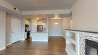 This single-floor unit offers a thoughtfully designed open-concept layout that seamlessly connects the kitchen, dining, and living areas. The kitchen is a standout feature, equipped with full stainless steel appliances including a range, microwave, refrigerator, and dishwasher. White shaker-style cabinetry pairs with granite-look countertops, while pendant lighting above the central island adds warmth and definition to the space. Wood-look plank flooring runs throughout the main living areas, contributing to a cohesive and modern aesthetic.

The living room is anchored by a built-in fireplace framed with mosaic tile and flanked by open shelving, providing both a functional focal point and ample display space. A sliding glass door with vertical blinds fills the room with natural light and offers access to an outdoor area. An adjacent dining space is illuminated by a decorative chandelier.

The bedrooms are carpeted for comfort, with neutral tones and natural light from windows with blinds. The bathroom features wood-look flooring, a white vanity with a granite-look countertop, a lighted mirror, and a dedicated laundry nook. Throughout the unit, clean lines, neutral wall colors, and consistent finishes create a calm, inviting atmosphere suited to everyday living.