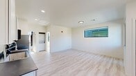Located at 1540 NW 30th St in Oklahoma City, Oklahoma, this efficiently designed one-bedroom, one-bathroom unit offers a clean, modern aesthetic across a single floor. Light wood-look flooring runs throughout the entire space, lending a bright and cohesive feel to every room. The open living area is illuminated by natural light through contemporary black-framed horizontal windows, creating an airy atmosphere despite the compact footprint. A well-appointed kitchen anchors one end of the main space, featuring white shaker-style cabinetry, dark countertops, and a full suite of stainless steel appliances including a refrigerator, range, microwave, and dishwasher. A stacked washer and dryer unit is also conveniently tucked into the living area. The bedroom receives ample natural light from a large window with outdoor views of surrounding greenery, and is equipped with a ceiling fan. The bathroom is finished with a white vanity, under-mount sink, chrome fixtures, a sleek black-framed mirror, and modern black hardware accents. Crisp white walls and recessed lighting throughout the space contribute to a fresh, contemporary ambiance that is both functional and inviting.