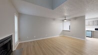 Located in Sandy Springs, GA, this two-story home offers a well-organized layout designed for comfortable living. The main level features a spacious living area with light hardwood flooring, neutral gray walls, and a classic fireplace flanked by two windows that allow natural light to pour in. A staircase leads to the upper level, adding vertical dimension to the open living space. The kitchen is thoughtfully equipped with gray raised-panel cabinetry, white countertops, and a full suite of stainless steel appliances including a refrigerator, gas range, dishwasher, and microwave. Additional storage and utility access are conveniently located just off the kitchen through louvered doors. Upstairs, the loft-style area is carpeted and bright, with multiple windows offering outdoor views and a ceiling fan overhead. A generously sized room on this level features light hardwood flooring, soaring vaulted ceilings with a textured finish, and a ceiling fan, creating an airy and versatile space. Throughout the home, consistent use of soft gray tones, white trim, and updated flooring contribute to a clean, cohesive aesthetic suitable for a variety of living arrangements.