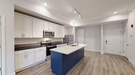 Located at 270 Lancer Dr in Nicholasville, Kentucky, this well-appointed single-floor residence showcases a thoughtfully designed open-concept layout with contemporary finishes throughout. The kitchen serves as the focal point of the living area, featuring crisp white shaker cabinetry, dark countertops, and a striking navy blue island with a white quartz surface and undermount sink. Stainless steel appliances, including a range, microwave, and refrigerator, complement the modern aesthetic, while track lighting and recessed fixtures provide ample illumination. Durable wood-look flooring extends throughout the main living and kitchen areas, creating a seamless flow. The living space is finished with crown molding, a ceiling fan, and access to a stacked washer/dryer area and electrical panel closet. Bedrooms are carpeted for comfort and feature windows that allow natural light to filter in. The primary suite connects to a walk-in closet outfitted with wire shelving for organized storage. The bathroom presents light tile flooring, white vanity cabinetry with brushed gold hardware, a large mirror, and a tub/shower combination. Clean, neutral wall tones throughout create a bright and cohesive ambiance.