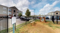 This residential community offers a thoughtfully designed layout that combines comfortable interior features with practical outdoor amenities. At the heart of the exterior amenities is a dedicated pet park, fully enclosed by black iron fencing for safety and security. The park includes a bench for owners to relax, agility tunnel equipment for pets, and a waste disposal station, all set on a natural ground surface. A signage board at the entrance outlines the park's guidelines. The surrounding building exteriors are finished with neutral lap siding and brick accents, reflecting a clean and cohesive architectural aesthetic throughout the community.

Inside, the space features a generously sized walk-in closet finished with soft carpet flooring, crisp white walls, and warm neutral paint tones. Wire shelving runs along the upper walls, providing ample storage and organization capacity. A classic six-panel interior door opens to an adjoining room, allowing for easy flow between spaces. The closet is well-proportioned, offering comfortable room to move and organize belongings. A utility connection point is also present within the space, adding functional versatility. Together, the indoor and outdoor elements of this community reflect a practical and pet-friendly living environment.