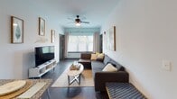 This single-floor residence offers a thoughtfully designed layout with multiple bedrooms, bathrooms, and shared living spaces that together create a comfortable and functional environment. The living room serves as the central gathering space, featuring dark hardwood-style flooring, a ceiling fan, large windows that allow natural light to fill the room, and a coastal-inspired aesthetic with tropical wall art and a generously sized sectional sofa. The galley-style kitchen is efficiently arranged with white cabinetry, granite countertops, stainless steel appliances including a dishwasher, and a stainless steel sink — providing ample workspace and storage. Each bedroom is individually styled, with ceiling fans, hardwood-style flooring, and accent walls in distinct colors including teal, green, and navy blue, giving each room its own character. One bedroom features a bright window with natural light and nautical-themed artwork, while another offers a dedicated study area with a desk. Each bathroom is well-appointed with granite vanity countertops, white cabinetry, large mirrors with overhead lighting, and shower-tub combinations. The consistent use of gray wall tones, granite surfaces, and wood-style flooring throughout ties the entire space together cohesively.