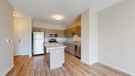 This single-floor residence offers a thoughtfully designed layout that balances functionality and contemporary style. The kitchen serves as a central highlight, showcasing warm taupe cabinetry with brushed nickel hardware, light granite countertops, and a full suite of stainless steel appliances including a refrigerator, range, microwave, and dishwasher. A freestanding center island provides additional prep space and serves as a natural gathering point, while light wood-look flooring ties the kitchen and adjacent living area together cohesively.

The bedroom is finished with plush wall-to-wall carpet and features a window that brings in natural light with views of greenery outdoors. A generously sized walk-in closet adjoins the bedroom, equipped with a full-width hanging rod and shelf, offering ample storage capacity. The bathroom continues the refined aesthetic with granite countertops, an undermount sink, shaker-style cabinetry with brushed nickel hardware, and a tub-shower combination. Neutral wall tones throughout the unit create a calm, versatile backdrop suitable for a variety of furnishing styles.
