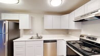 Located at 401 E Magnesium Rd in Spokane, WA, this thoughtfully updated 2-bedroom, 1-bathroom unit offers a functional single-floor layout with modern finishes throughout. The combined kitchen and living area forms the heart of the home, where the kitchen impresses with crisp white shaker-style cabinetry, bright white quartz-style countertops, stainless steel appliances including a dishwasher and electric range, and a single-basin sink. The living room features warm luxury vinyl plank flooring that carries throughout the unit, a textured ceiling, and a sliding glass door that fills the space with natural light and provides direct outdoor access. Both bedrooms are comfortably proportioned with neutral gray walls, LVP flooring, windows with blinds, and baseboard heating. The primary bedroom includes a dedicated closet with sliding panel doors. The bathroom is clean and functional, featuring a full tub-shower combo with built-in shelving, a white vanity, and matching fixtures. Additional spaces include a utility room and a dedicated closet, providing practical storage solutions. The unit presents a cohesive, move-in-ready aesthetic with updated interiors throughout.